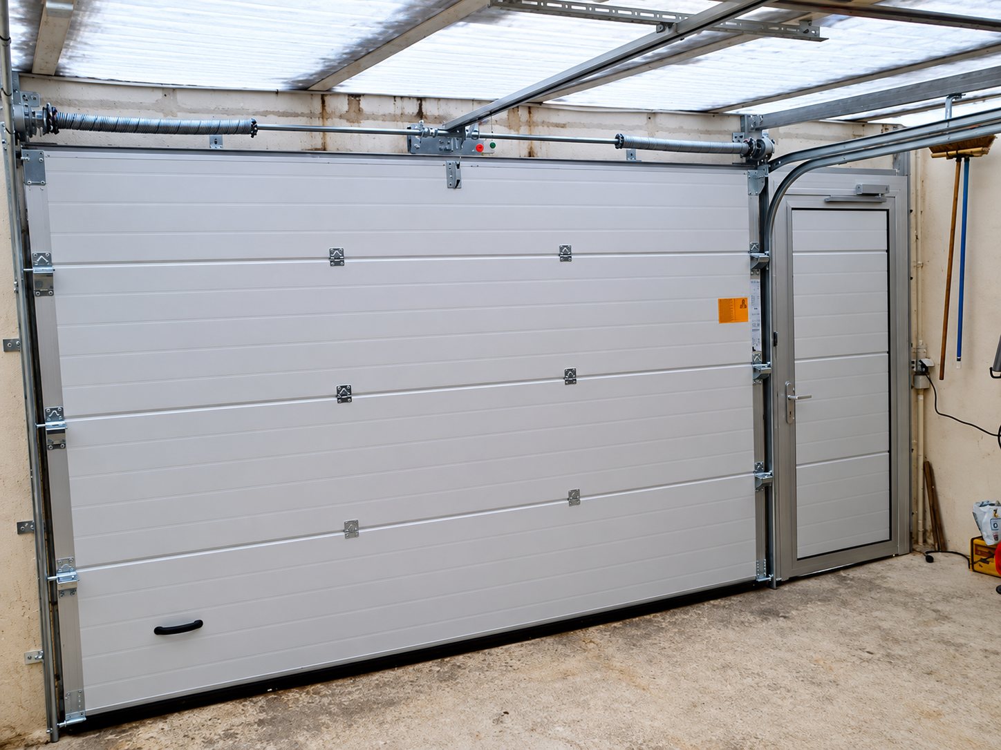 Vue intérieure d'un garage équipé d'une porte sectionnelle grise à panneaux horizontaux avec un portillon intégré sur la droite.