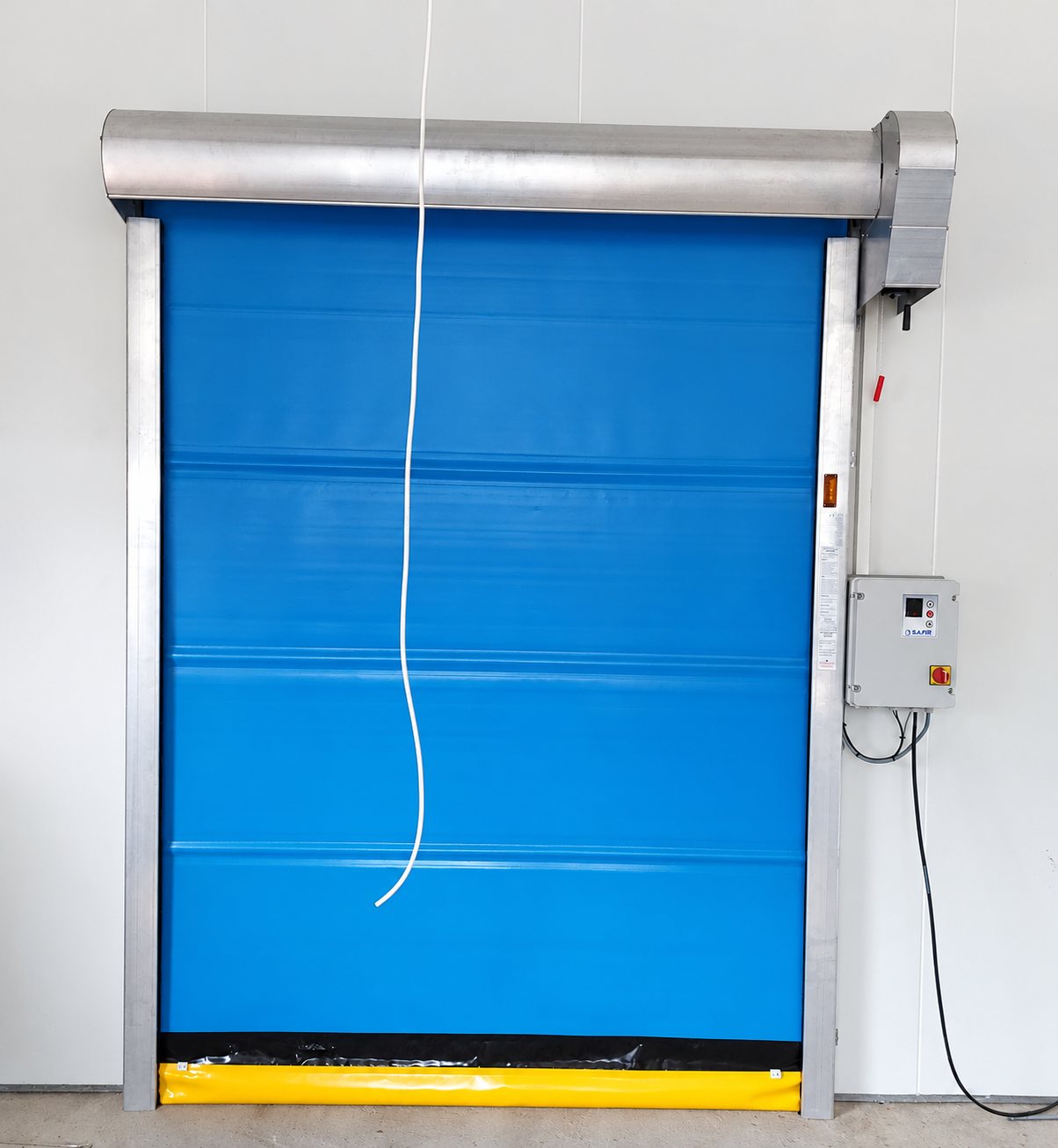 Porte rapide à enroulement bleue avec bas jaune, caisson en aluminium et coffret de commande gris fixé au mur blanc d'un local industriel.